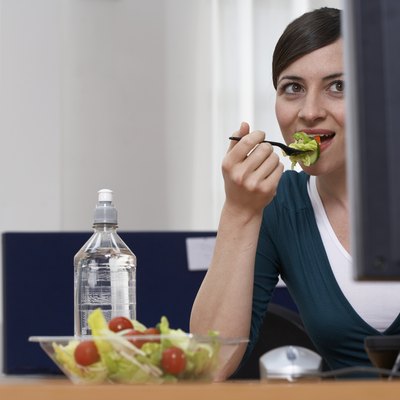 Woman eating salad at desk in office