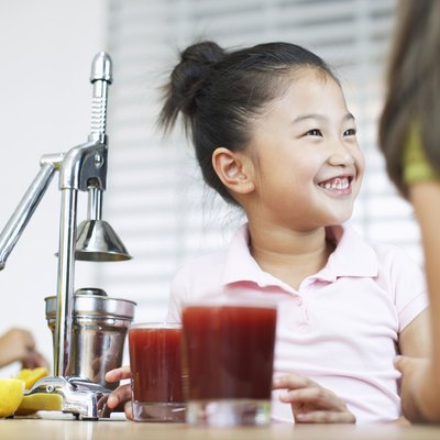 Girl (5-7) in kitchen grinning by juice