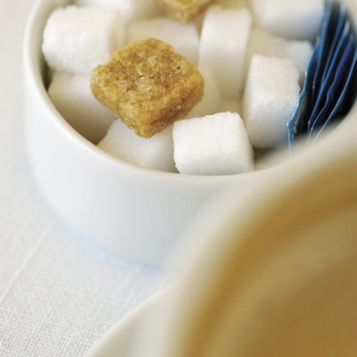 Sugar bowl with sugar cubes next to cup of cappuccino