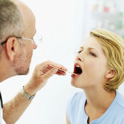 male doctor examining a young woman's throat with a tongue depressor