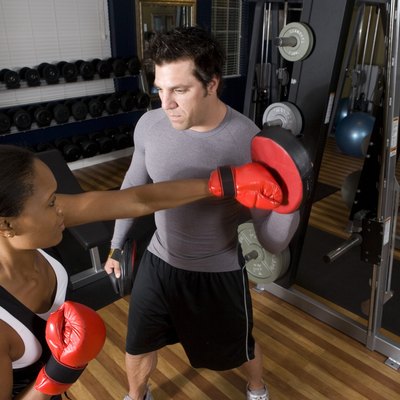 Trainer instructing a young woman with boxing equipment in the gym