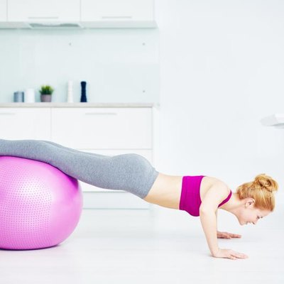 Girl doing push-ups in the kitchen with her legs on fitball