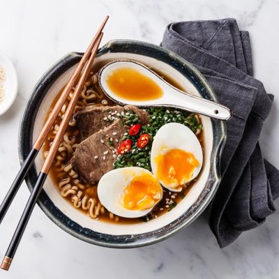 Miso ramen Asian noodles with beef and egg in bowl on white marble background.