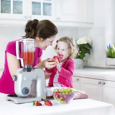 Laughing toddler girl and beautiful mother in sunny white kitchen