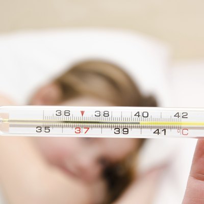 Mother holding thermometer foreground and sick little girl