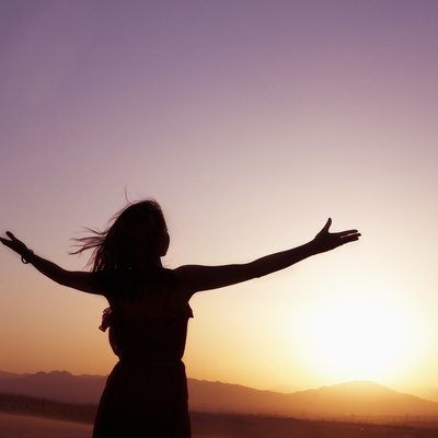 Serene young woman with arms outstretched doing yoga in the desert in China, Silhouette