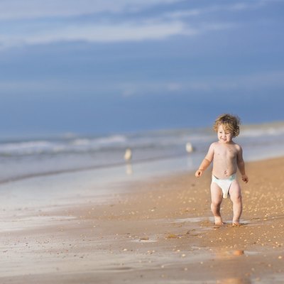 Cute baby girl with curly hair running on beautiful beach