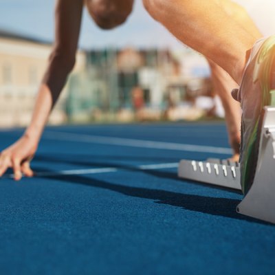 Feet on starting block ready for a spring start. Focus on leg of a athlete about to start a race in stadium with sun flare.