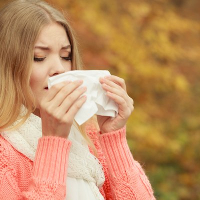 Sick ill woman in autumn park sneezing in tissue.