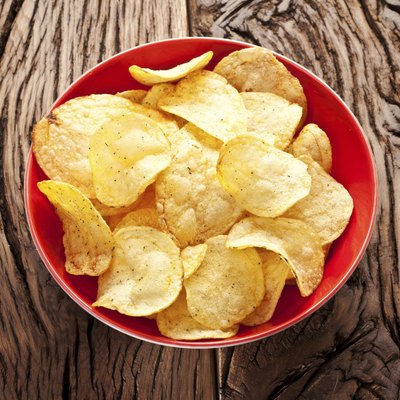 Potato chips in a bowl on old wooden table.