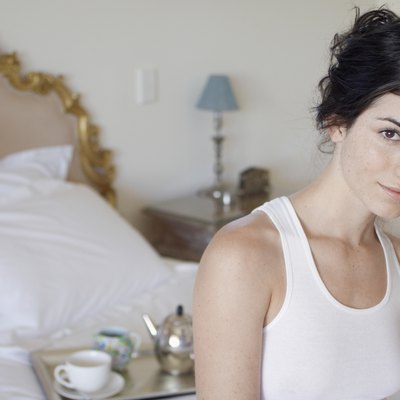 Young woman drinking orange juice on bed (portrait)