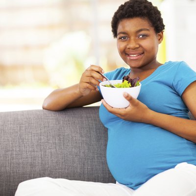 pregnant african woman eating green salad on sofa