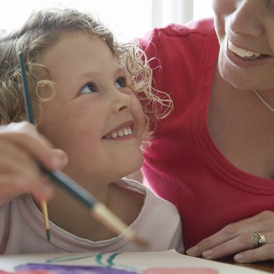 "Girl (3-5) painting picture, looking up at mother, smiling"
