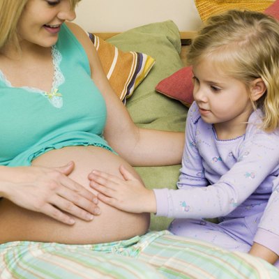 Girl (4-5) sitting on bed touching belly of pregnant mother, close-up