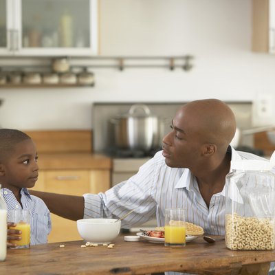 Father and son (5-7) looking at each other at breakfast table