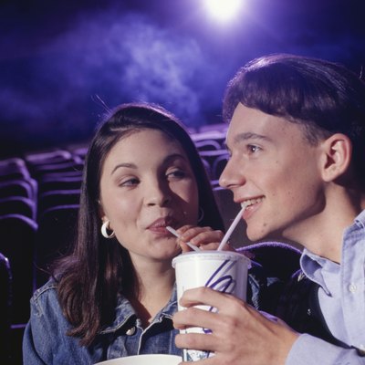 Teenage couple (16-17) sitting in cinema with popcorn, sharing soda