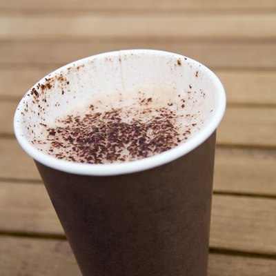 Cappuccino coffee in disposable cup on wooden table, close-up