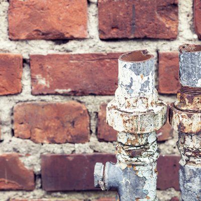 Old rusty cut pipes on a brick wall background.