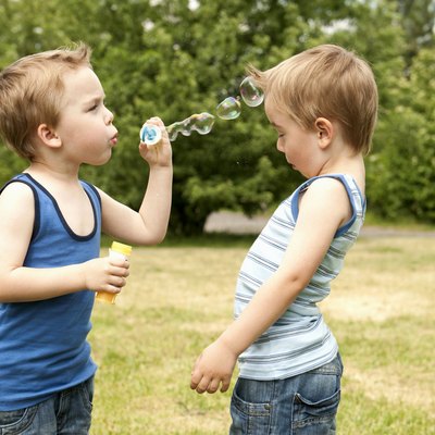 Twin blowing bubbles at brother in park