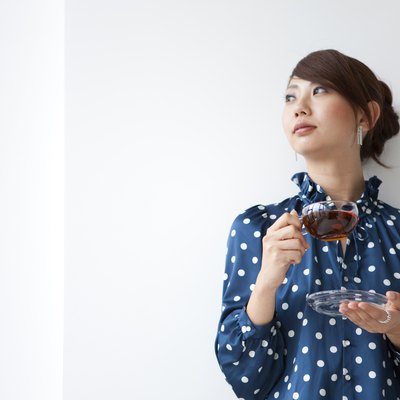 Young woman leaning on wall and looking away, holding cup of tea, white background, copy space