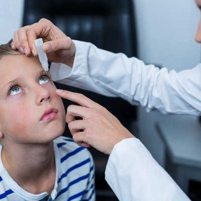 Female optometrist putting eye drop in young patient eyes