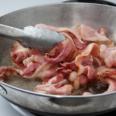 Sizzling bacon in a pan on the stove being stirred