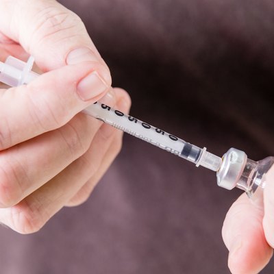 Syringe drawing insulin from vial
