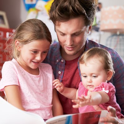 Father Reading Book With Daughters In Bedroom