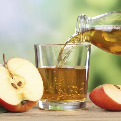 Apple juice pouring from red apples into a glass