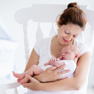 Young mother and newborn baby in white bedroom