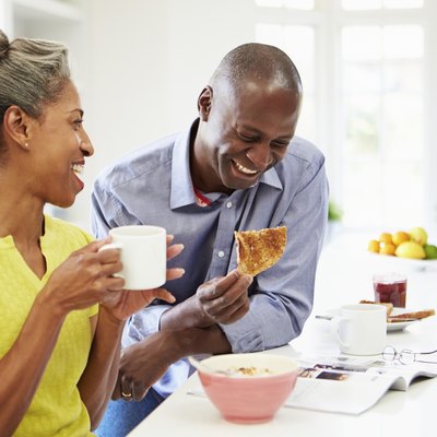 Couple Having Breakfast And Reading Magazine In Kitchen
