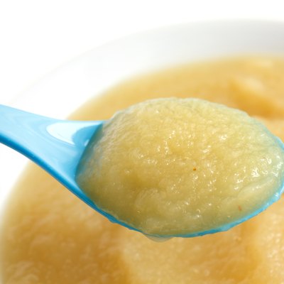 White dish of apple sauce with blue baby spoon.