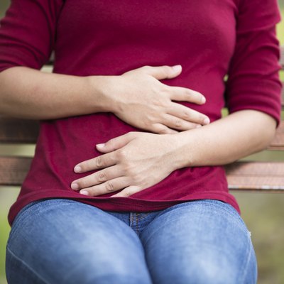 Woman Has Stomach Ache Sitting on Bench at Park