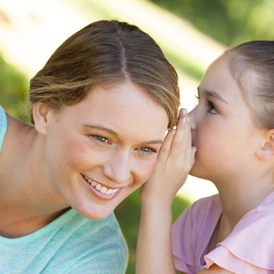 Girl whispering secret into mother's ear at park