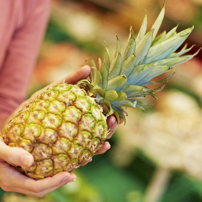 Germany, Cologne, Young woman with pineapple in supermarket