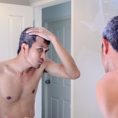 Man worried about gray hair while looking into a mirror.