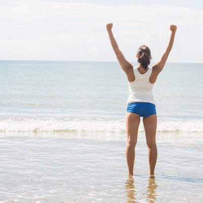Lovely slim woman standing on beach raising her arms