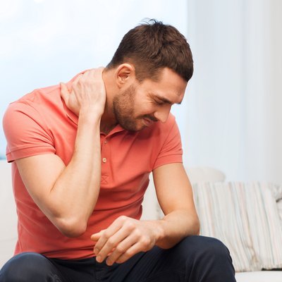 unhappy man suffering from neck pain at home
