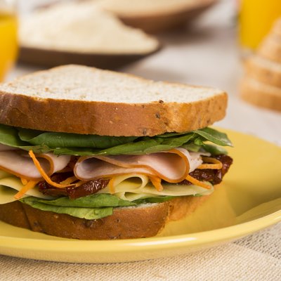 Sandwich on a white plate with turkey breast, tomato, lettuce.