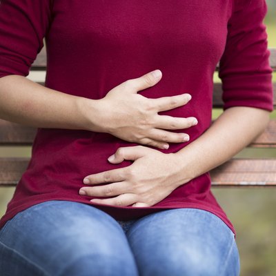Woman Has Stomach Ache Sitting on Bench at Park