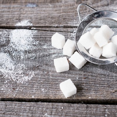 Lump sugar in a metal strainer s on wooden background.