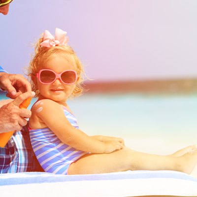 father applying sunblock cream on daughters shoulder