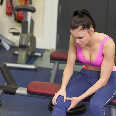 Healthy woman with an injured knee sitting in gym