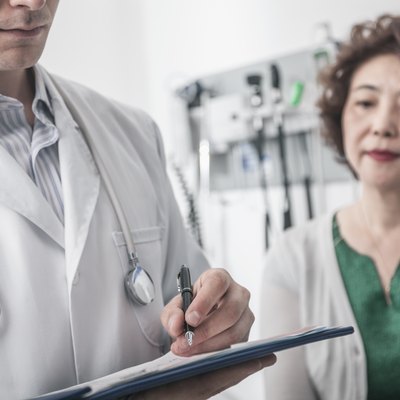 Doctor writing on medical chart with patient in the background