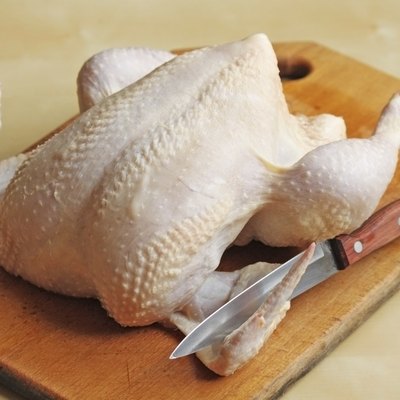 Whole raw chicken on the chopping board with a knife