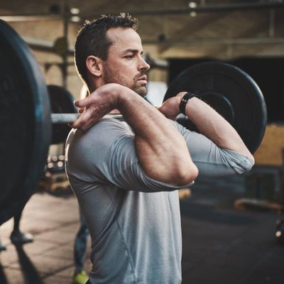 Tough bearded man with thick muscular arms and gray shirt pulling up large barbell in fitness training class indoors