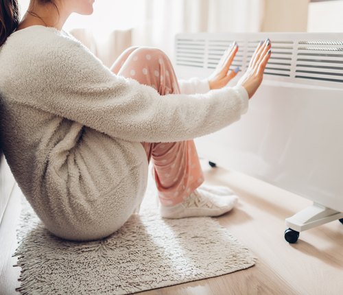 person with cold hands warming up by heater
