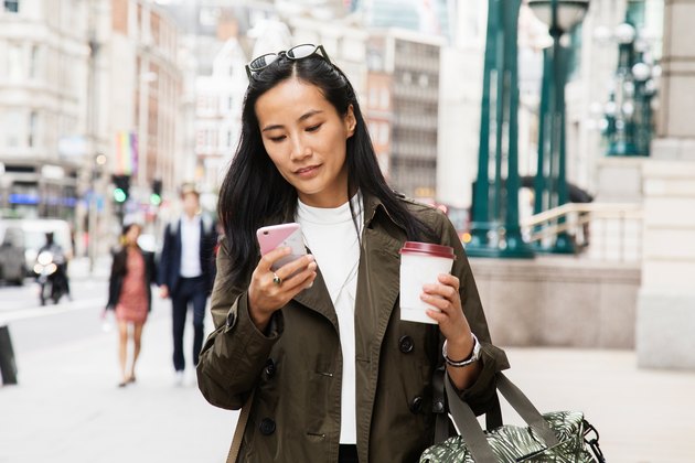 Woman walking down a busy city street looking at her phone.