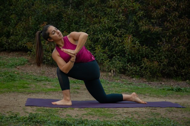 Woman performing twisting low lunge on yoga mat.