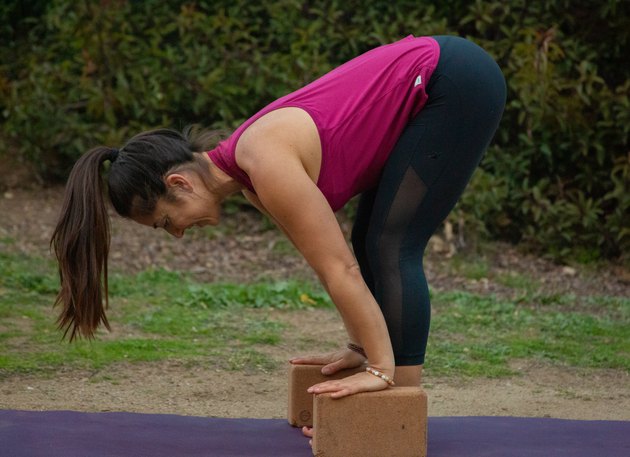 Woman performing forward fold with hands on yoga blocks.